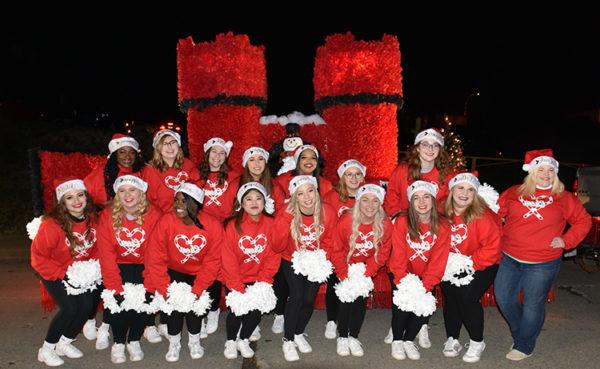 W&J Cheerleaders pose in front of the parade float students put together for the Washington Holiday Parade. 